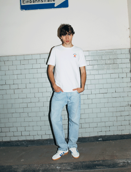 Kim steht vor einer gemauerten Wand und er trgt eine hellblaue Jeanshose, weie Sneaker und seine Oberteile wechseln in mehreren aufeinander folgenden Bildern in verschiedenen Lagenlooks von T-Shirt, ber Pullover, zu Hemd, bis Weste und Schal; Zu Oberteile gehen